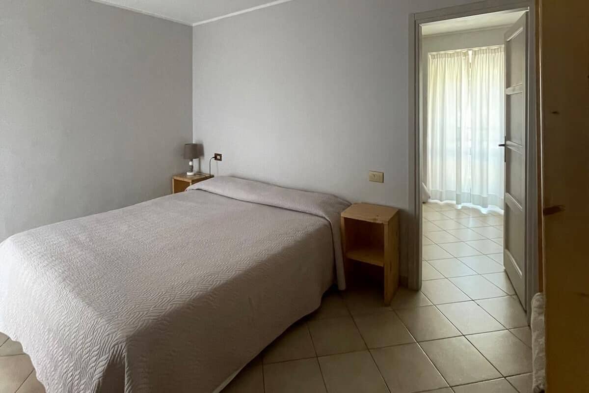 Une pièce simple et épurée, comprenant un lit, une table de chevet, une lampe et une porte donnant sur une autre pièce.