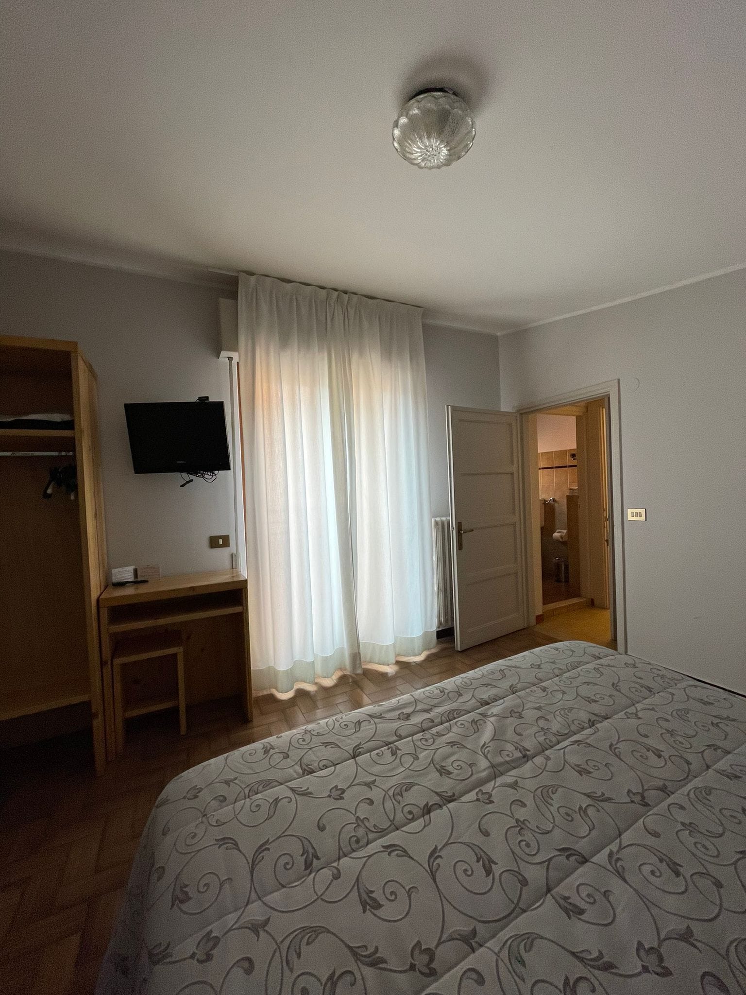 Een hotelkamer met een bed, een bureau, een televisie en een deur naar een badkamer.