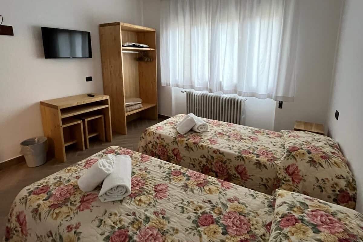 Une chambre d’hôtel avec deux lits, une télévision, une armoire en bois, un radiateur et une fenêtre avec des rideaux.