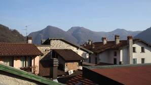 A traditional European village with stone buildings, red-tiled roofs, and a mountainous backdrop.
