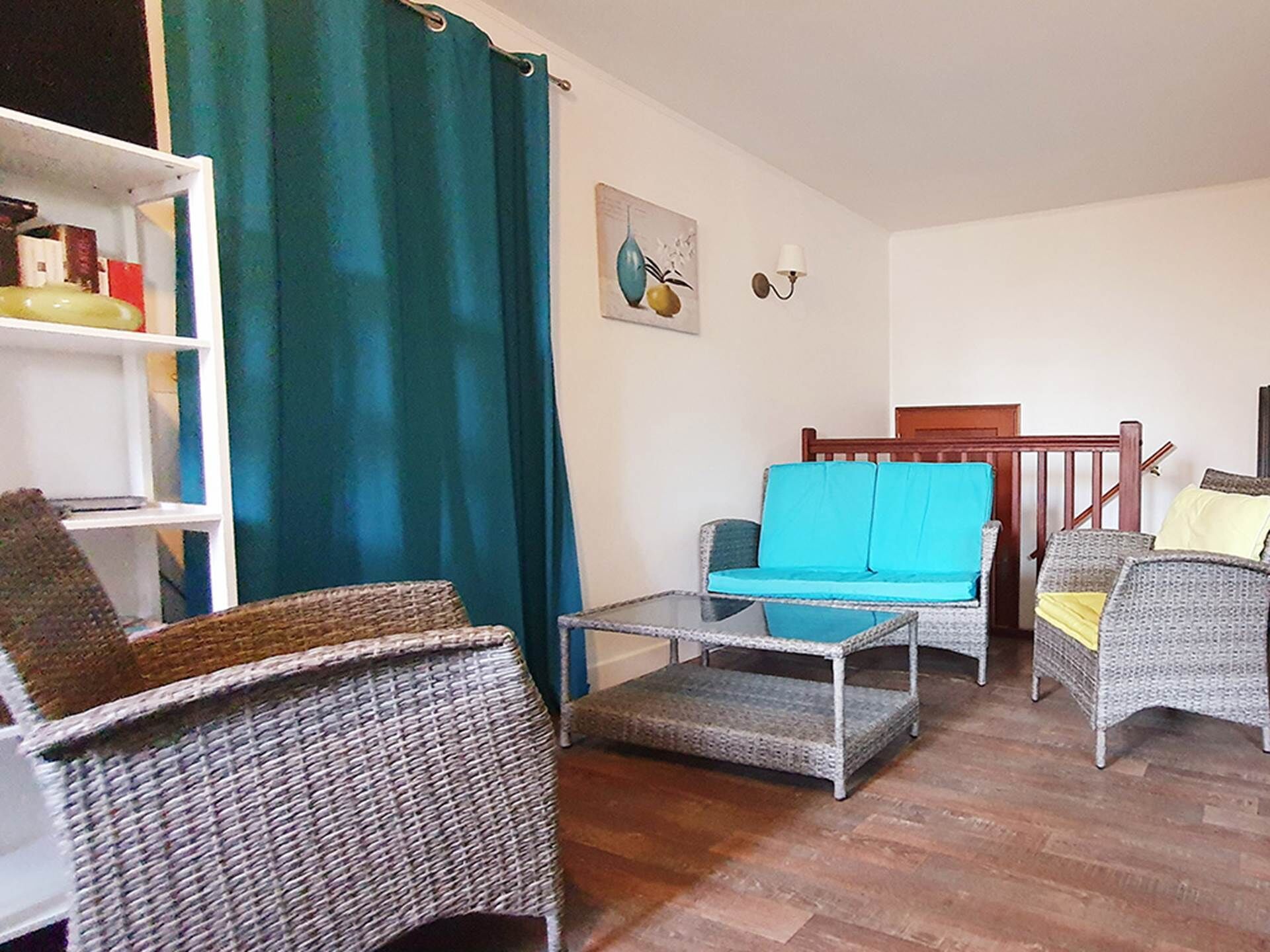 Un salon avec des meubles en osier, un canapé de couleur turquoise et une chaise en bois.
