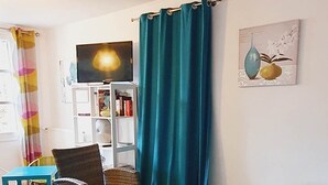 A furnished living room with wicker furniture, a glass coffee table, and a teal curtain. - Le Colombard, cosy B&B (CONDOM)