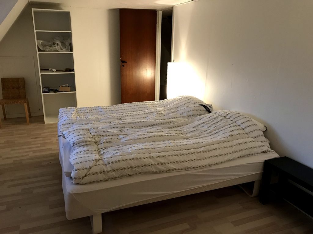 A bedroom with a bed, a wooden door, a white wardrobe, and a chair.