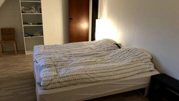 A bedroom with a bed, a wooden door, a white wardrobe, and a chair.