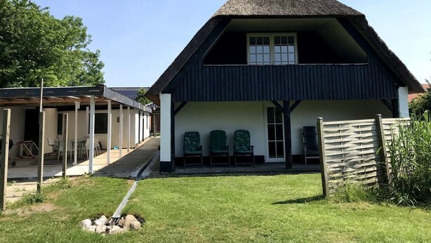 A building with a thatched roof, a covered porch with chairs, and a grassy yard. - Schönes Ferienhaus in Strandnähe (Rødekro)