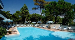 A swimming pool with lounge chairs and umbrellas, surrounded by trees. - Hotel Imperiale (Cervia)