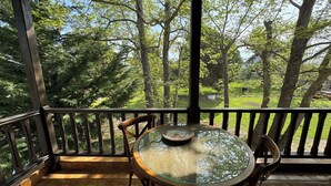 A covered outdoor area with a round glass table and chairs, surrounded by a wooden railing and a view of a green landscape with trees. - La maison des vacances - Vourvourou Sithonia (Vourvourou)