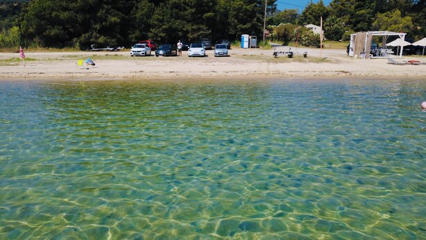 A beach with clear water, a sandy shore, and parked cars. - La maison des vacances - Vourvourou Sithonia (Vourvourou)