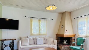 A living room with a sofa, a wooden coffee table, a fireplace, a television, and a window with curtains. - La maison des vacances - Vourvourou Sithonia (Vourvourou)