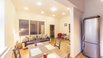 Ein modernes Wohnzimmer mit Esstisch für zwei Personen, einer Couch, einem roten Sessel und einem großen Fenster.