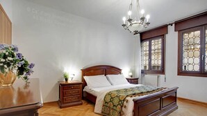 A bedroom with a wooden bed, nightstands, a chandelier, and a window with a decorative grille. - Grimaldi Apartments - Elena (Venice)