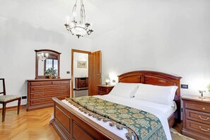 A bedroom with a wooden bed, a dresser, a chair, a mirror, and a chandelier. - Grimaldi Apartments - Elena (Venice)