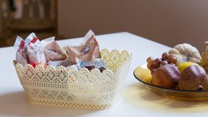 A table with a lace basket containing packaged food items and a glass bowl with various fruits and pastries. - Grimaldi Apartments - Elena (Venice)
