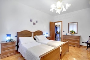 Una habitación de hotel con cama doble, cabecero de madera, mesitas de noche con lámparas, cómoda y candelabro.
