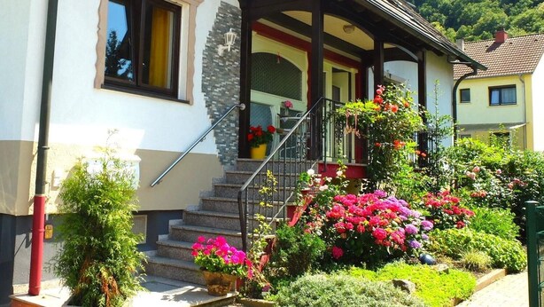 Una casa de dos pisos con porche, escaleras y un jardín lleno de flores.