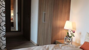 Habitación de hotel con cama, mesita de noche con lámpara, armario de madera y espejo.