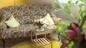 Una habitación con un sofá estampado con motivos florales, una pequeña mesa auxiliar de madera con un jarrón de flores y una lámpara amarilla.