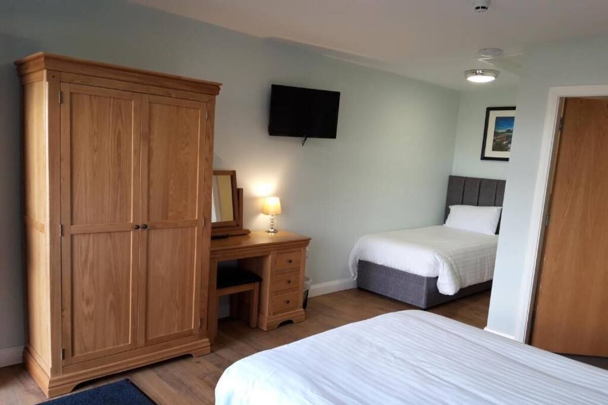 A bedroom with a bed, a wardrobe, a desk with a lamp, and a television on the wall.
