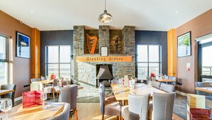 A restaurant with a stone fireplace, wooden tables, and grey upholstered chairs. - Standing Stones Lodge (Belfast)