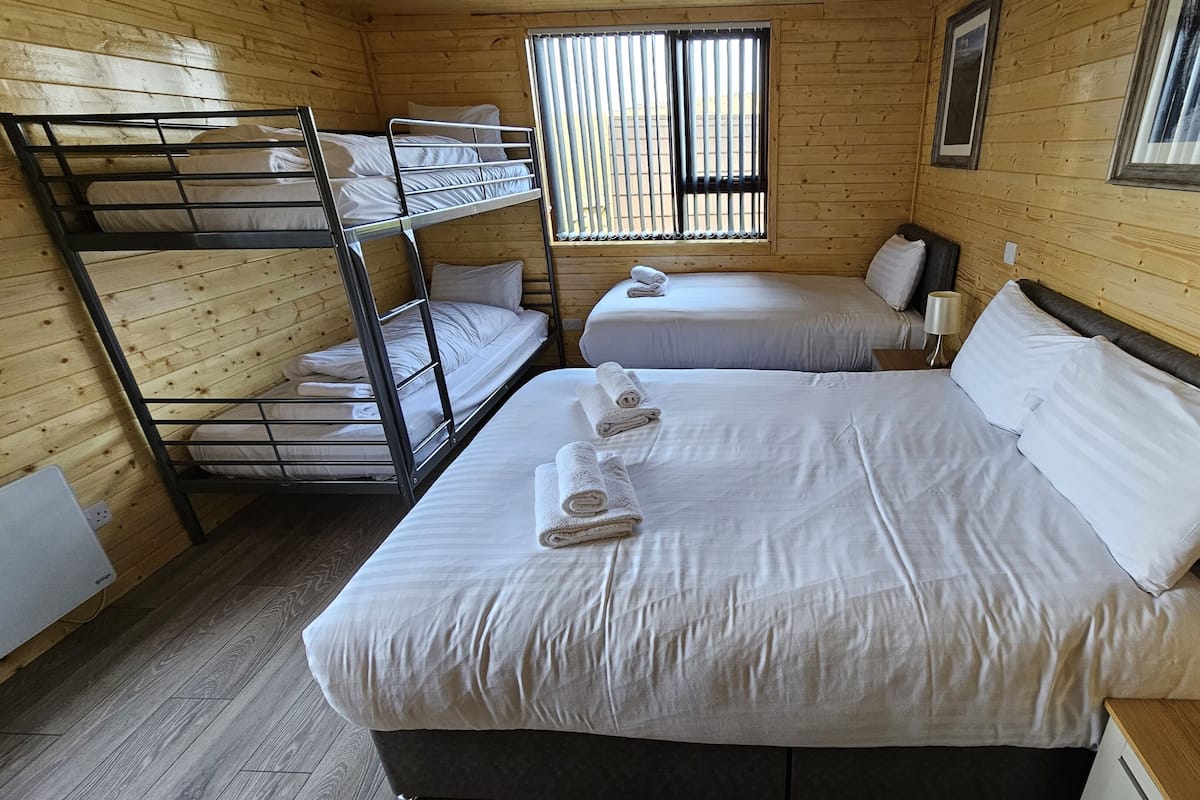 A wooden cabin room with bunk beds, a single bed, and a window with blinds.