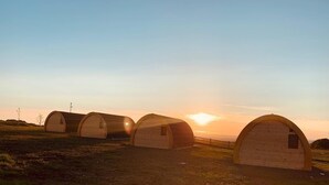 A row of wooden dome-shaped cabins with a sunset in the background. - Standing Stones Lodge (Belfast)