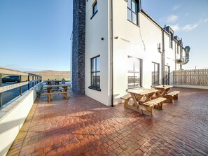 A patio area with wooden tables and benches, a stone wall, and a view of the road. - Standing Stones Lodge (Belfast)