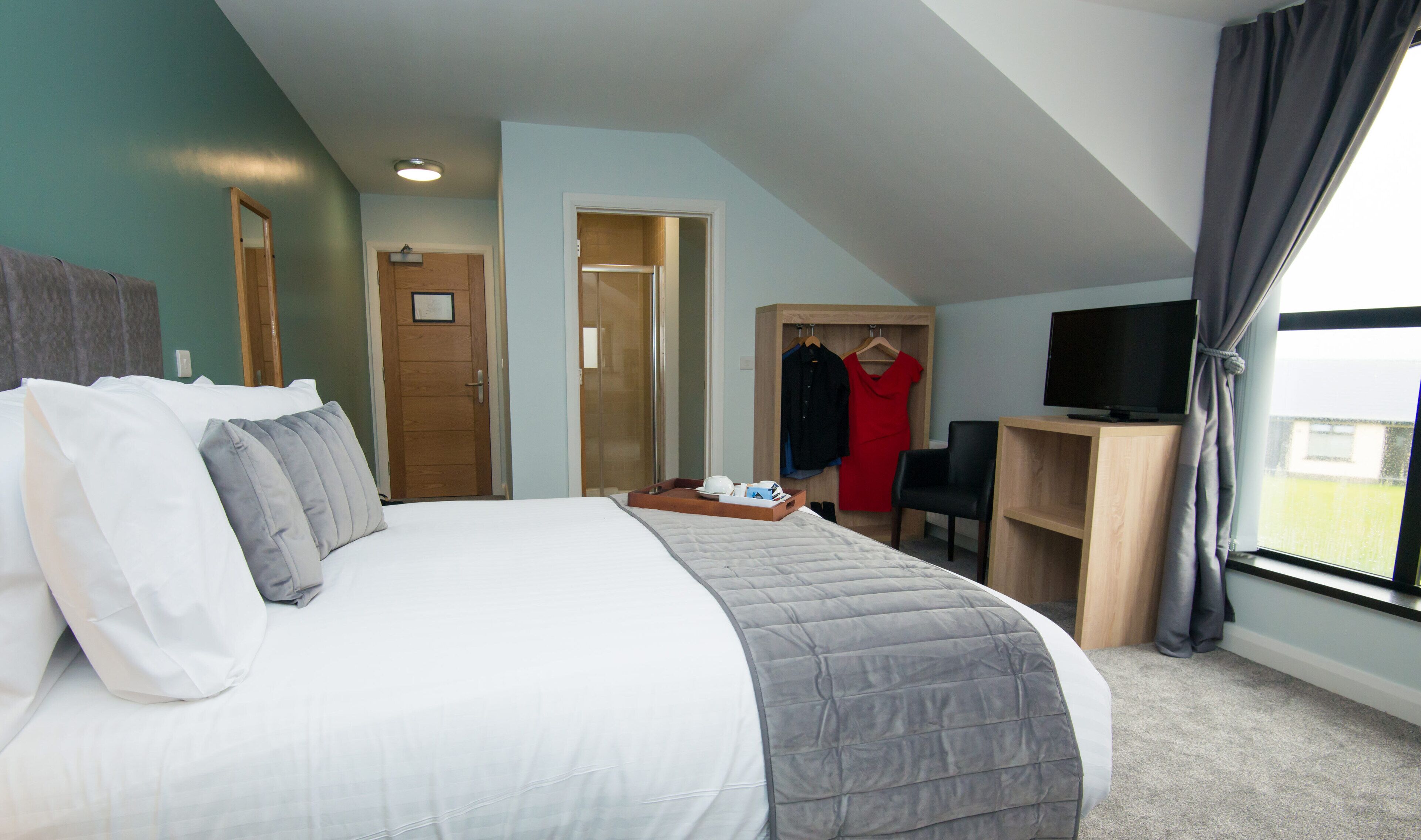 A hotel room with a large bed, a desk, a TV, and a wardrobe.