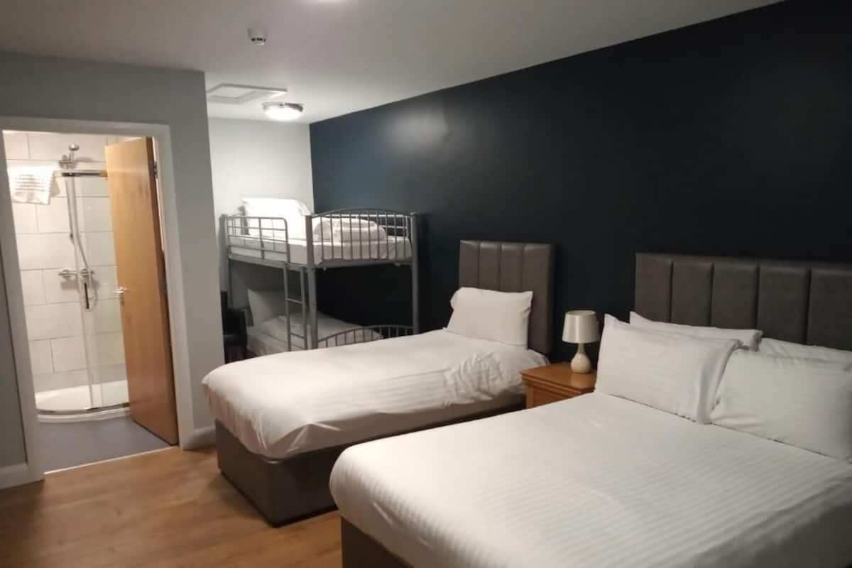 A hotel room with two beds, a shower area, and a dark wall.