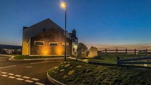 A modern building with a stone facade and a flat roof, surrounded by a well-maintained lawn and a wooden fence. - Standing Stones Lodge (Belfast)