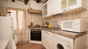 A compact kitchen with white cabinets, a built-in oven, a microwave, and a washing machine. - Grimaldi Apartments - San Marco Economy (Venice)