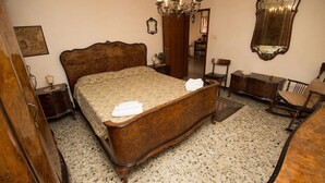 A bedroom with a large wooden bed, a wooden dresser, a chair, a mirror, and a chandelier. - Grimaldi Apartments - San Marco Economy (Venice)