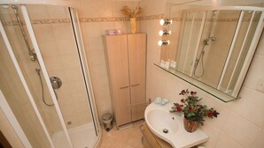 A bathroom with a glass shower enclosure, a wooden cabinet, a sink with a mirror above, and a small potted plant. - Grimaldi Apartments - San Marco Economy (Venice)