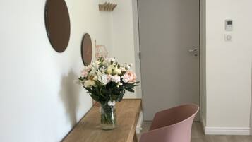 A dining area with a wooden table, a vase of flowers, a pink chair, and a door in the background.