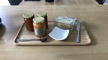 A wooden table with a tray holding two jars of jam, a container of cream, a spoon, and a knife.
