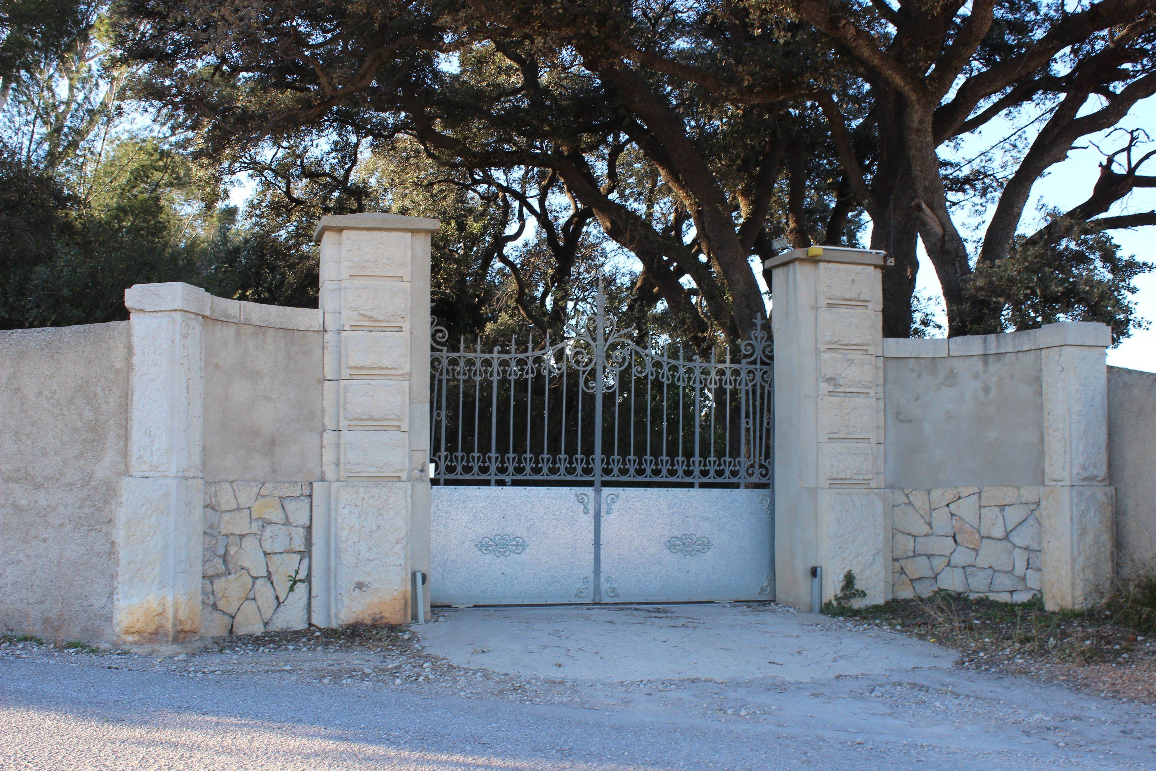 Una entrada cerrada con muro de piedra y portón de metal, rodeada de árboles.