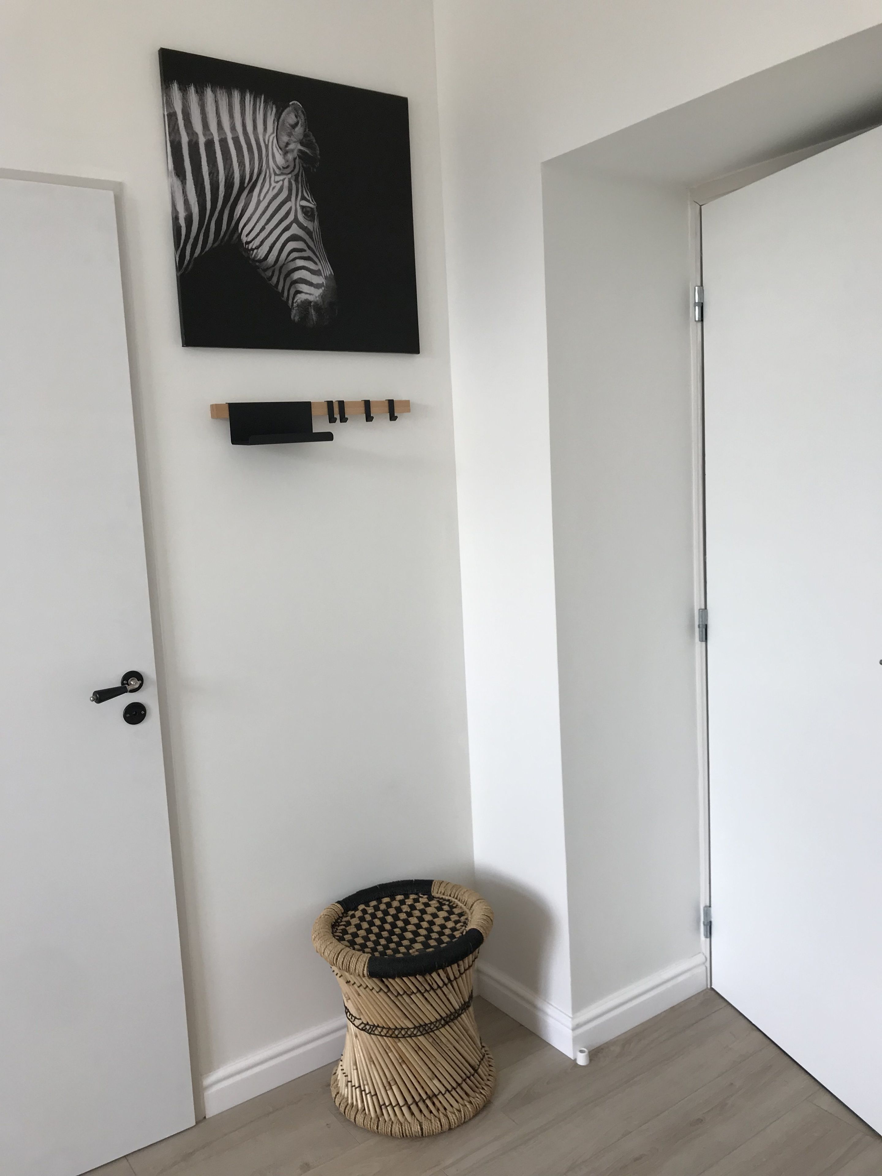 A room with a white door, a zebra-themed artwork, a blackboard, and a woven stool.