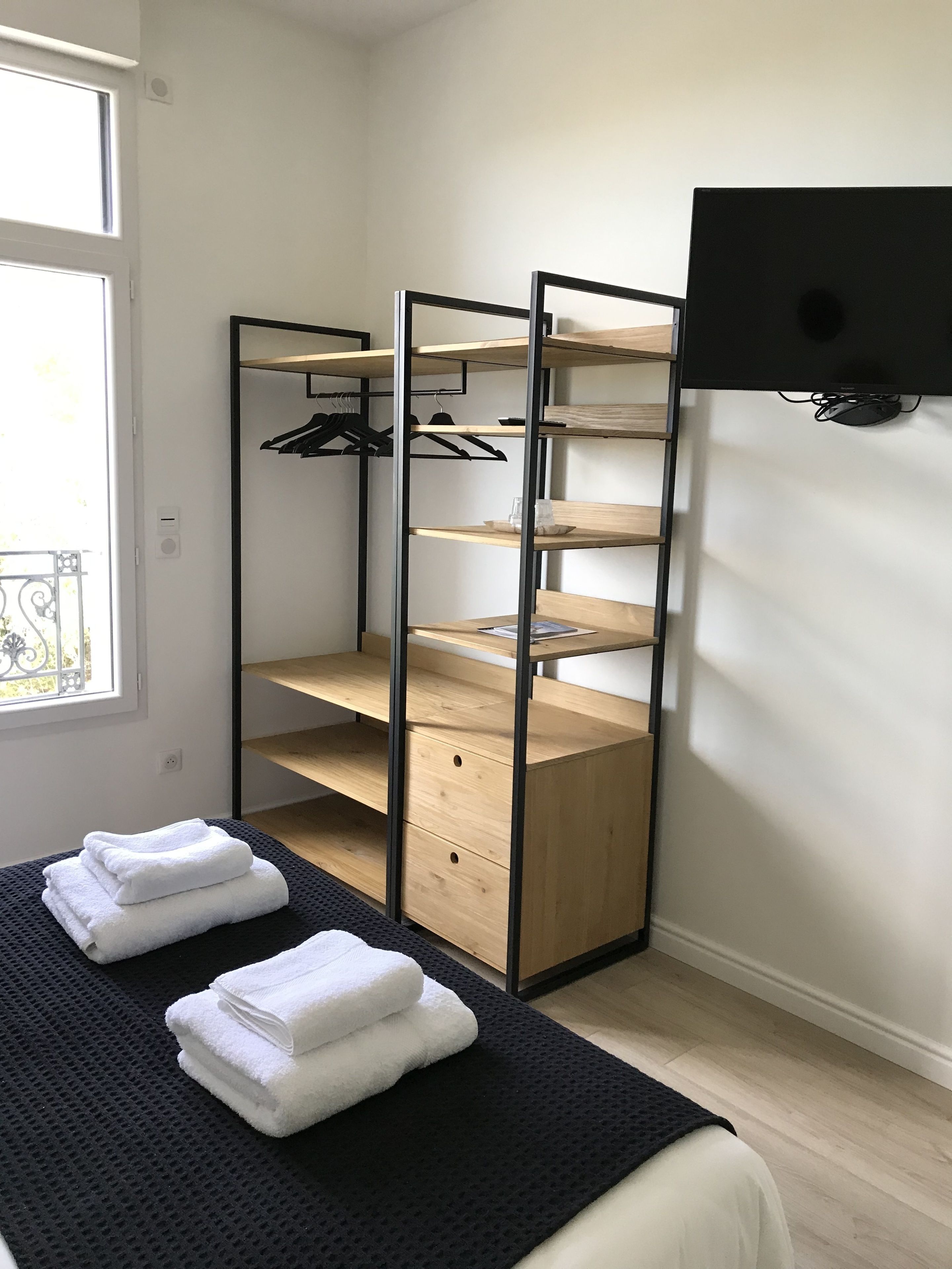 Een slaapkamer met een bed, een kledingkast met veel planken, een aan de muur bevestigde televisie en een raam met uitzicht.