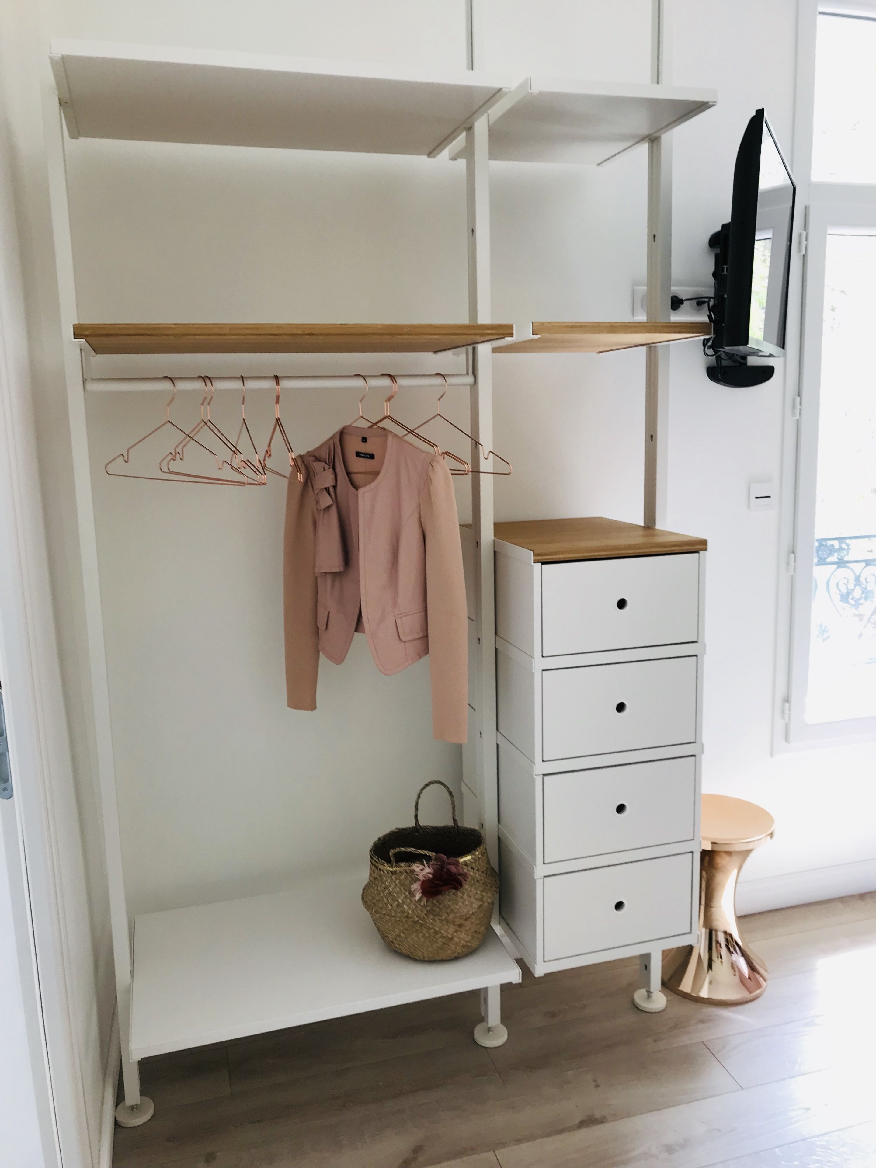 A white wardrobe with multiple shelves, a hanging rod, and a small table with a basket.