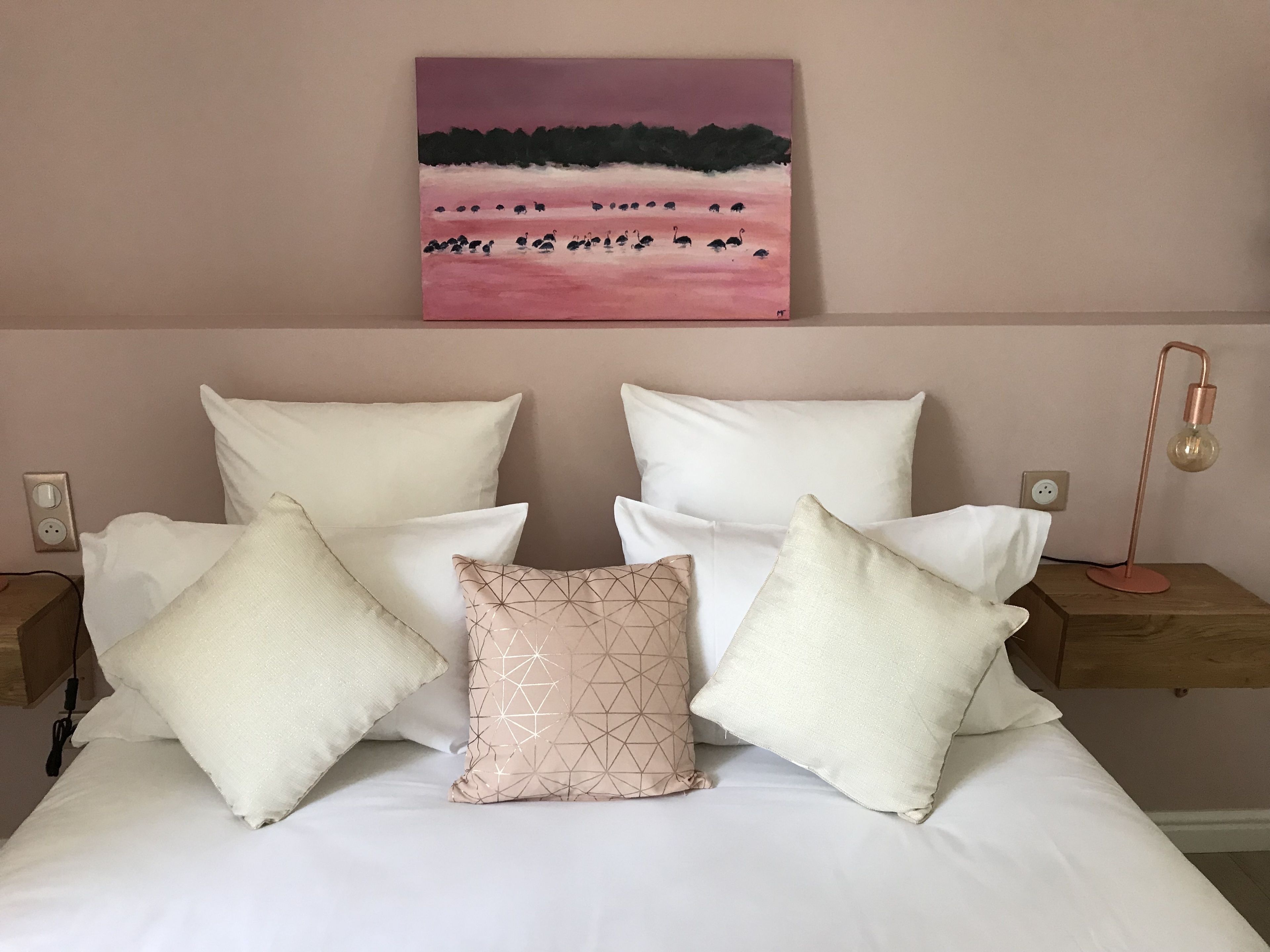 A neatly made bed with multiple pillows, a bedside lamp, and a painting on the wall.