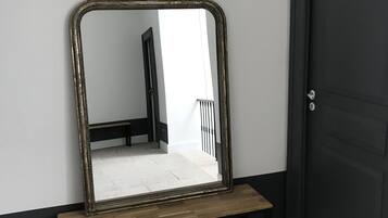 Un miroir posé sur un support en bois, adossé à un mur, avec une porte sur la droite.