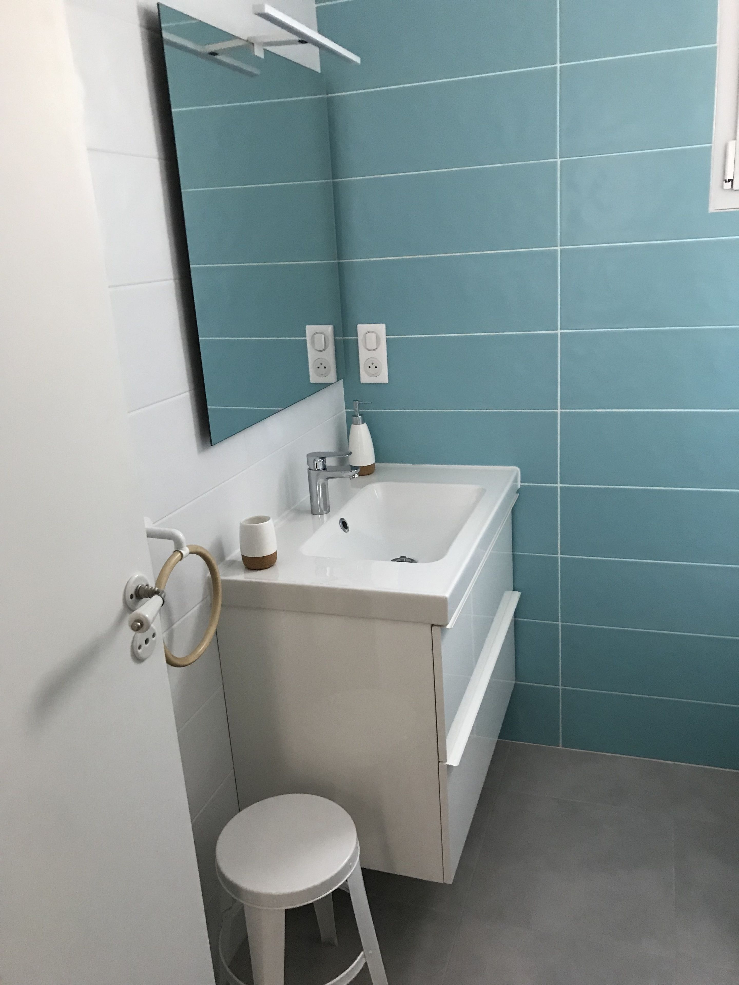 Un baño con un lavamanos blanco, un espejo y un inodoro. Hay dos enchufes en la pared.