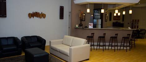 A modern living room with a sofa, ottoman, and chairs, a kitchen area with bar stools, and a wooden floor.