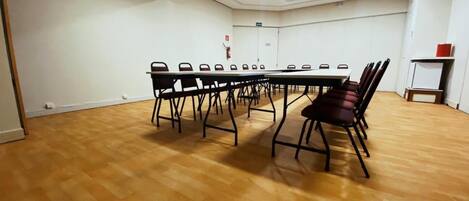 A conference room with a long table and chairs, white walls, and wooden flooring.