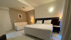 Une chambre d’hôtel avec un grand lit, une table de chevet, une lampe, un canapé et un petit tableau accroché au mur.