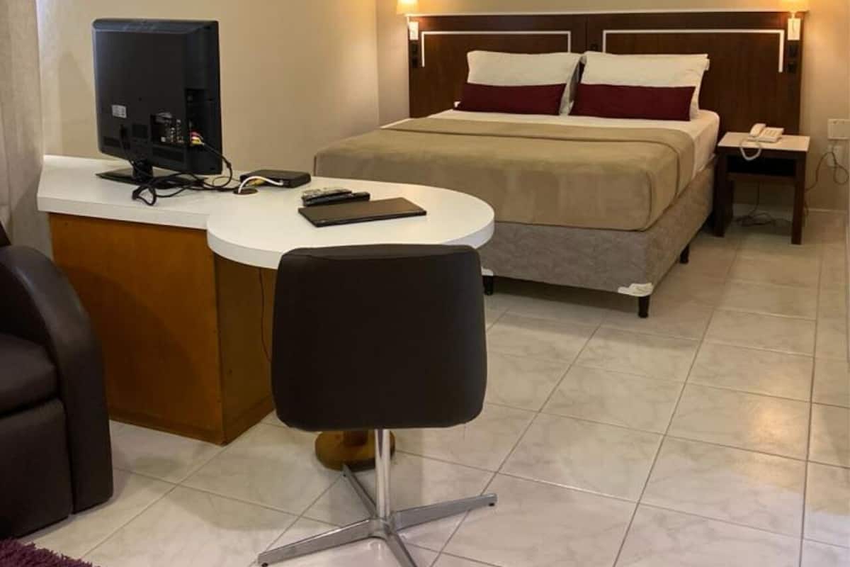 A hotel room with a bed, bedside table, chair, desk with computer, and a telephone.