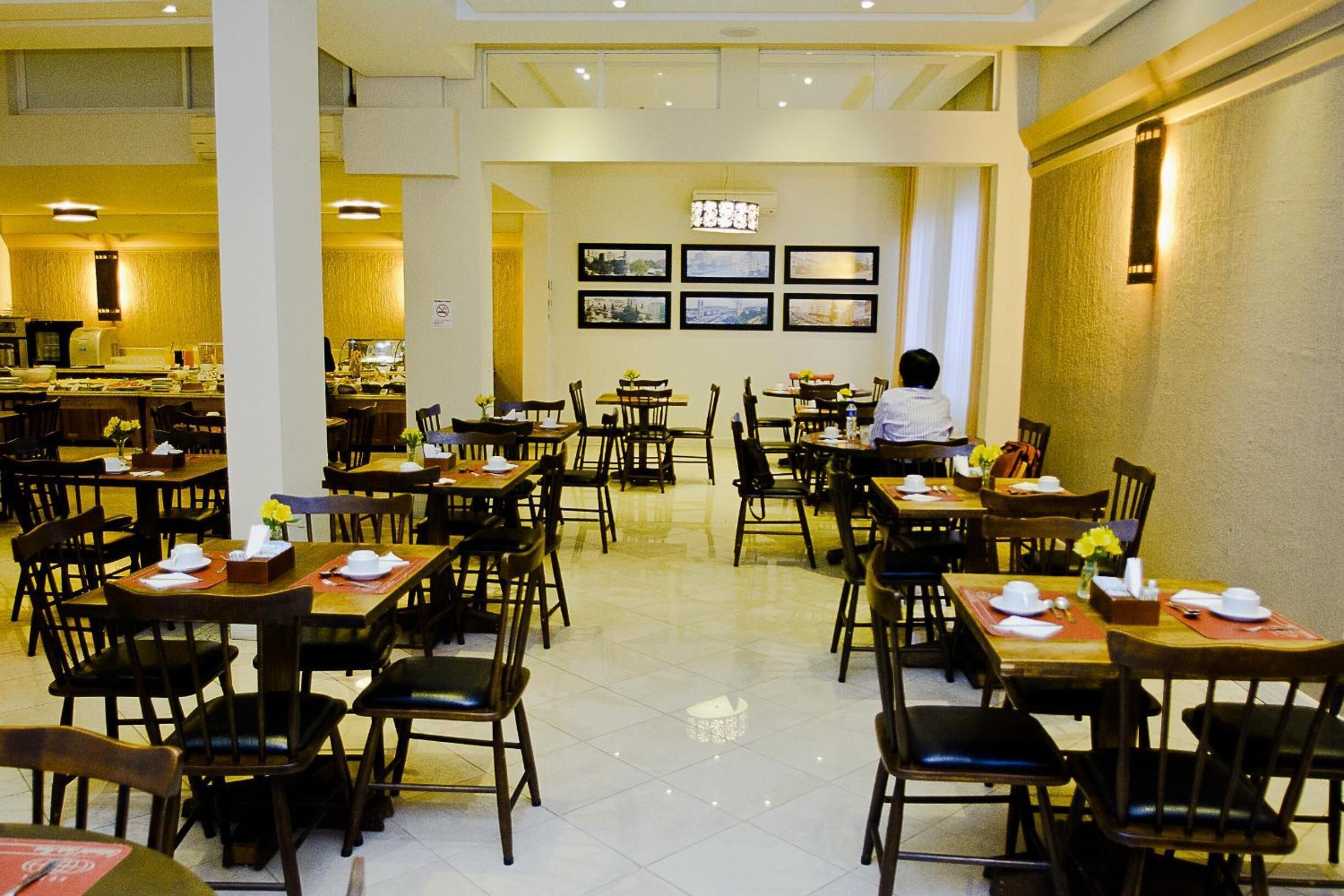 Un comedor amplio con varias mesas y sillas, un pasillo central y cuadros en las paredes.