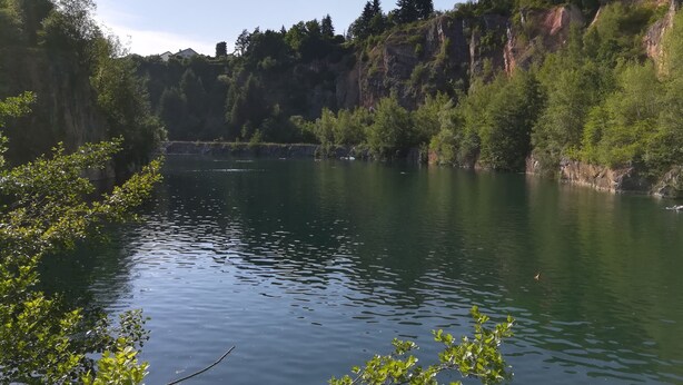 Ein ruhiger Fluss mit dichtem Grün und felsigen Klippen im Hintergrund.