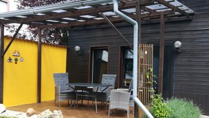 Eine Terrasse mit Tisch und Stühlen, eine gelbe Wand und ein Holzzaun.