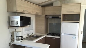 A compact kitchen with a microwave, stove, sink, and refrigerator. - Camping Pen Guen (Saint-Cast-le-Guildo)
