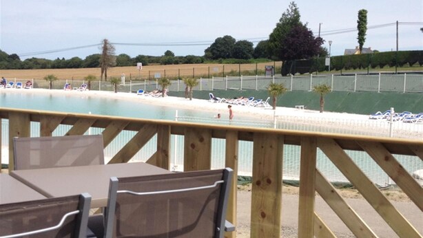 A poolside area with a wooden deck, lounge chairs, and a view of the pool and beach. - Camping Pen Guen (Saint-Cast-le-Guildo)
